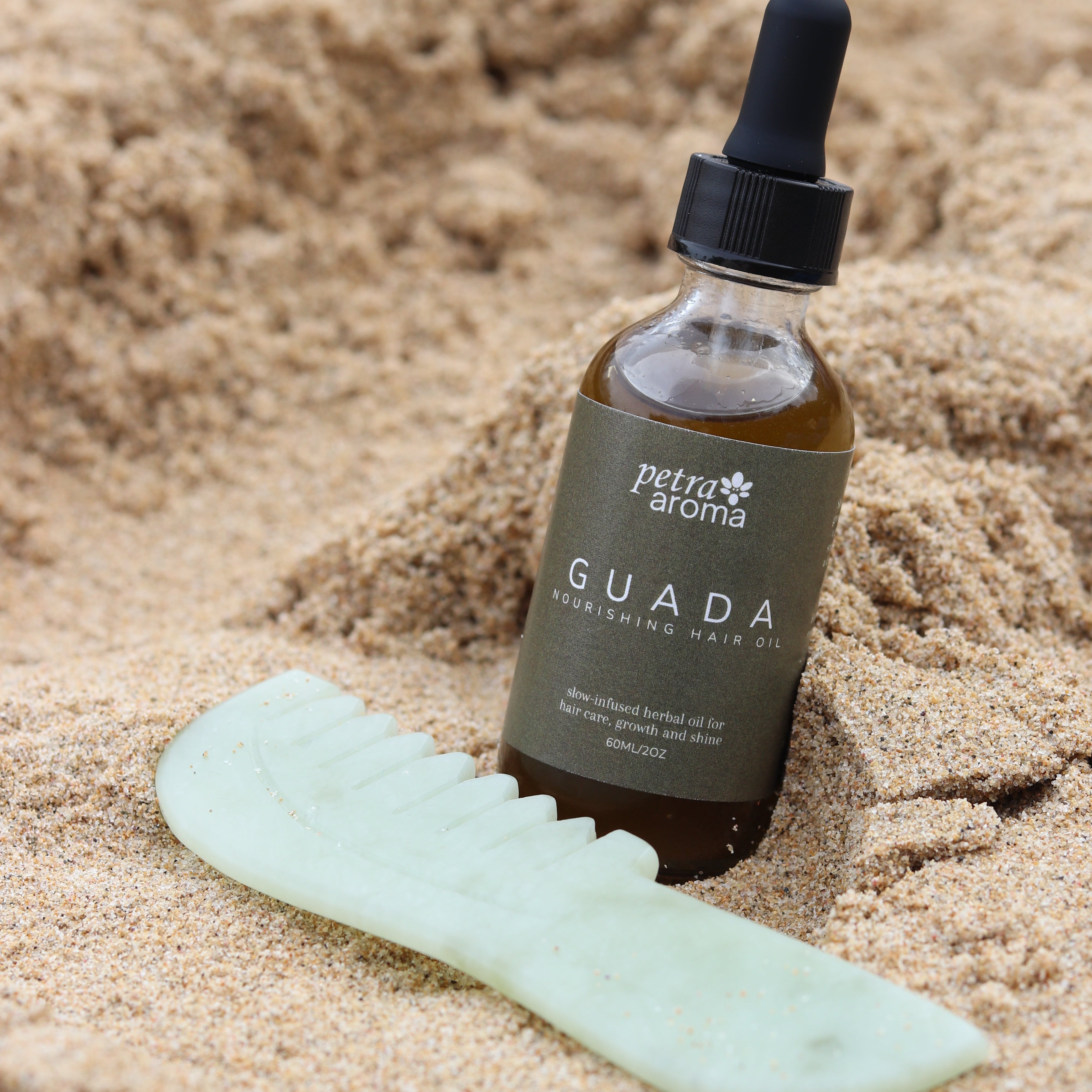 Bottle of Guada skincare product on sand with a green tool