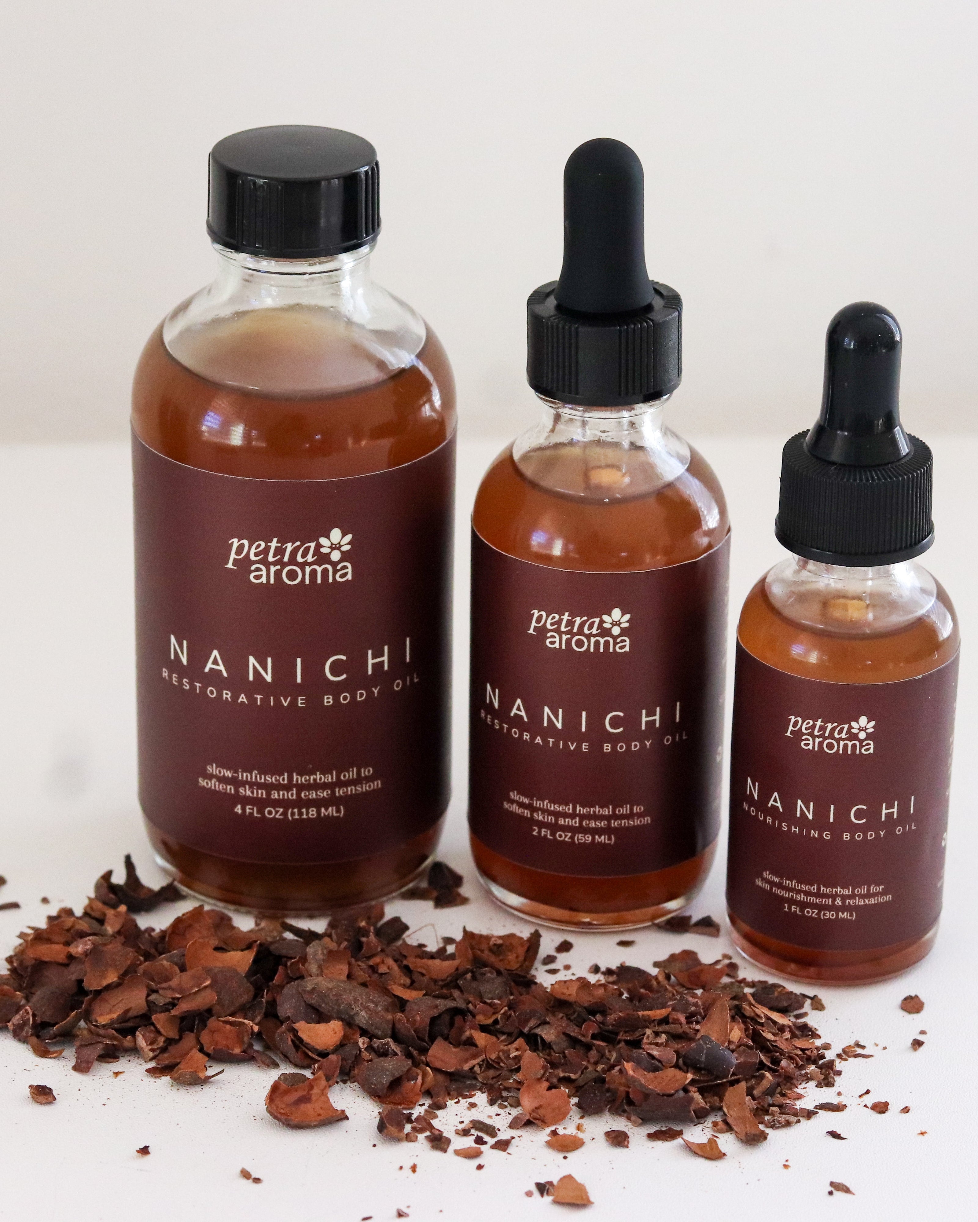 Three bottles of Petra Aroma Nanichi body oil on a white background with cocoa beans.