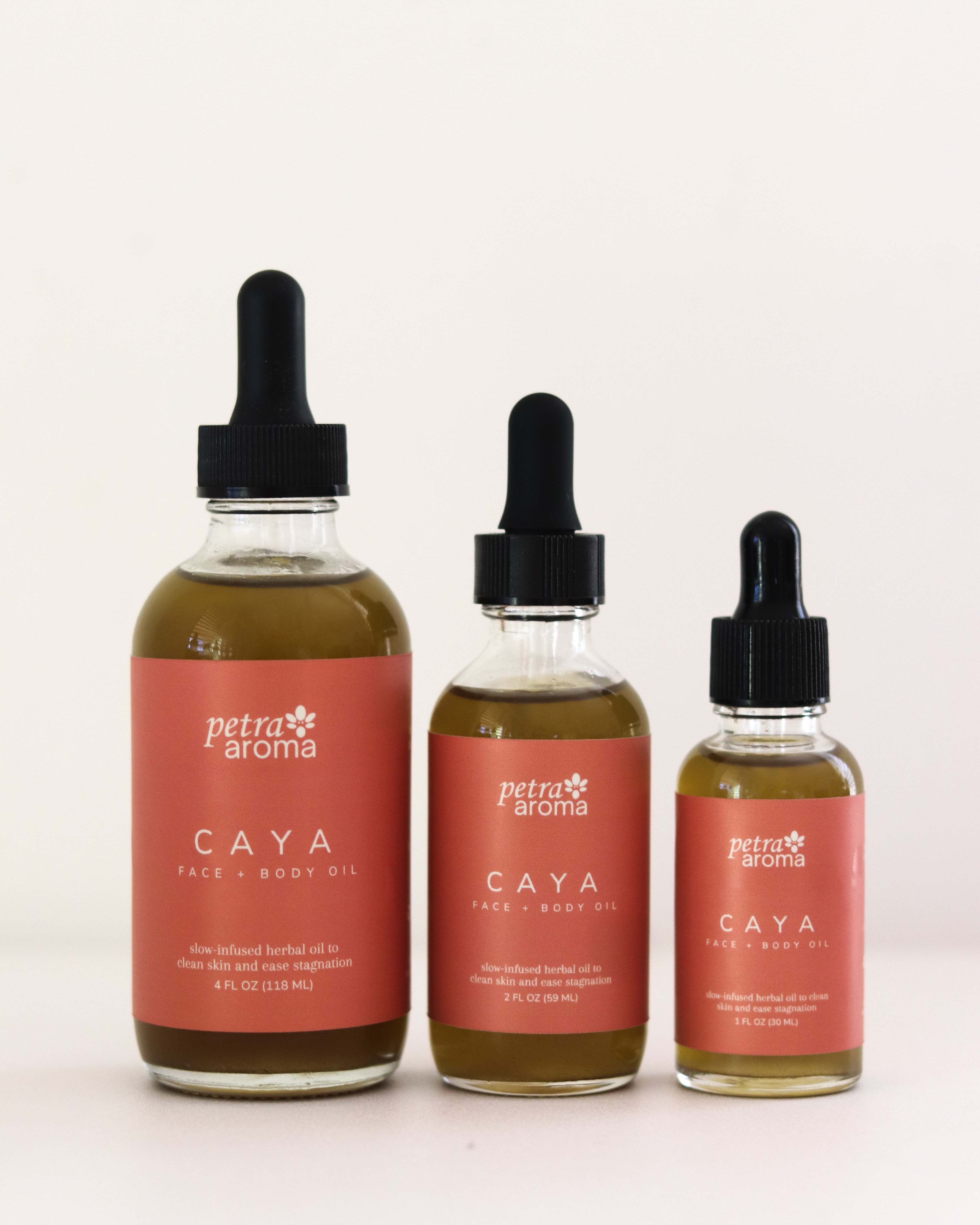 Three bottles of Petra Aroma Caya hair and body oil on a white background