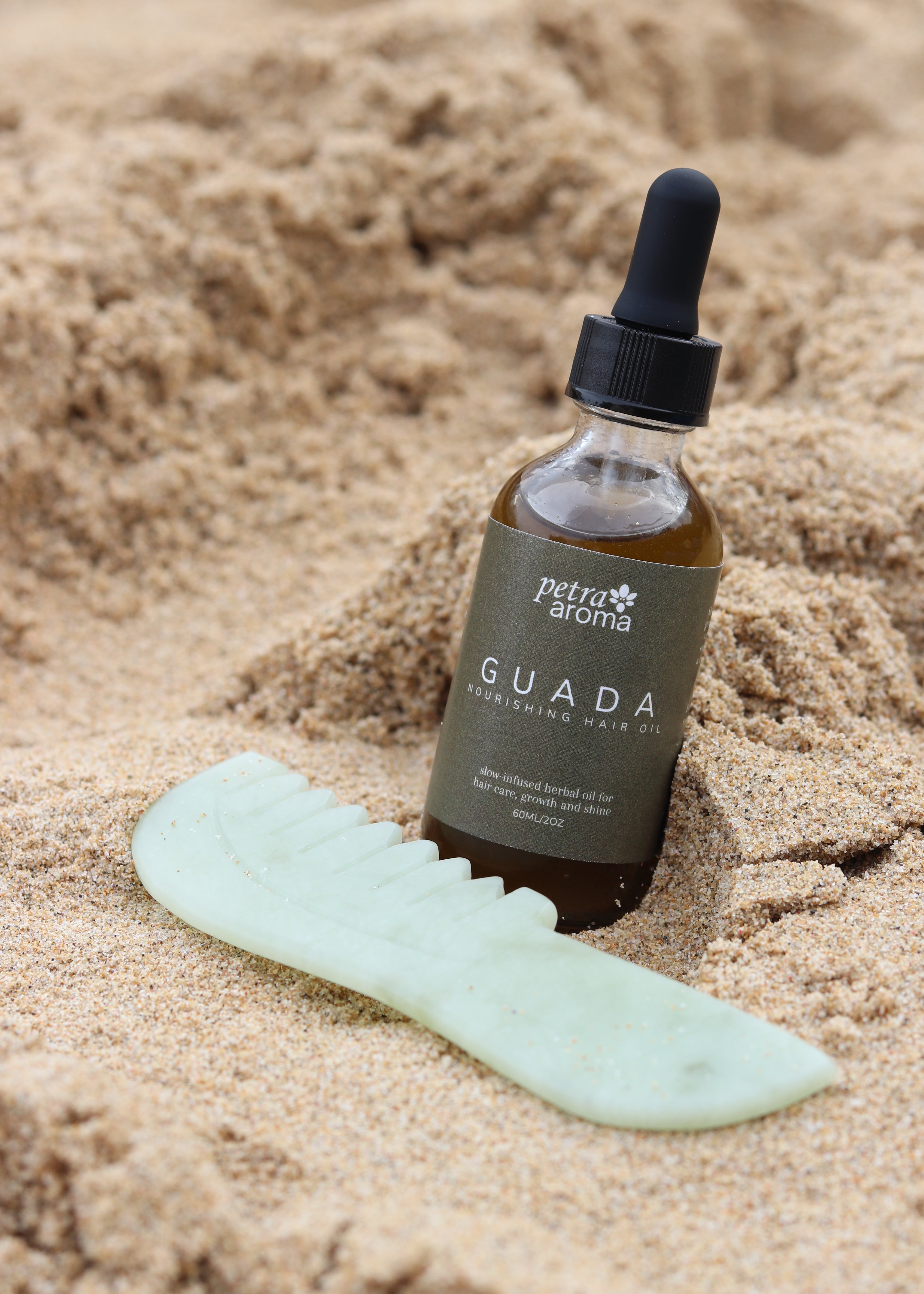 Bottle of Guada skincare product on sand with a green tool