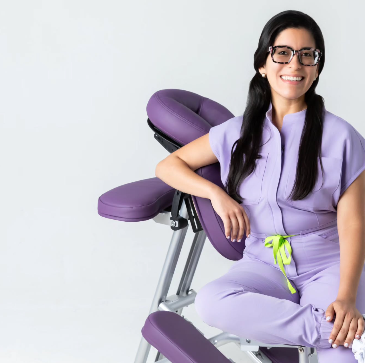 Woman in a purple uniform sitting on a massage chair against a white background